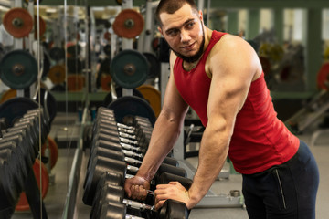 Fototapeta na wymiar Guy working out in the gym. Strong man takes dumbbells for training.