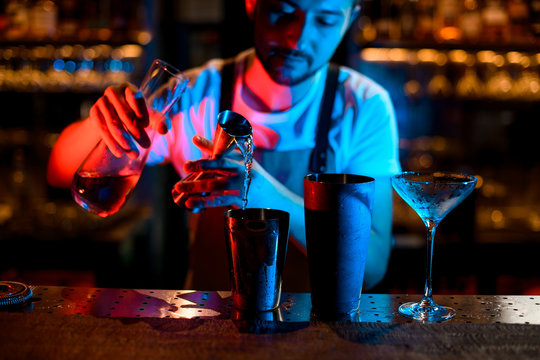 Bartender pours cocktail with jigger in neon lights