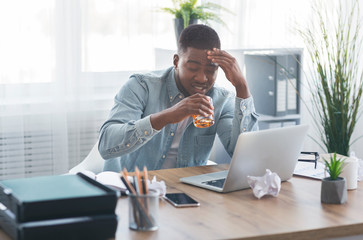 Tired black businessman drinking alcohol at workplace