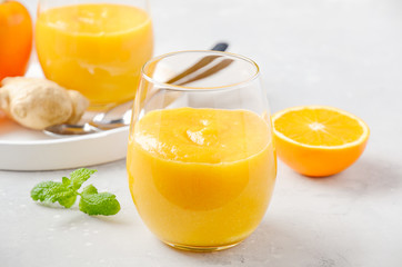 Fresh healthy smoothie with persimmon, orange and ginger on gray concrete background.