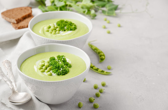Green pea soup in bowls on gray concrete or stone background.