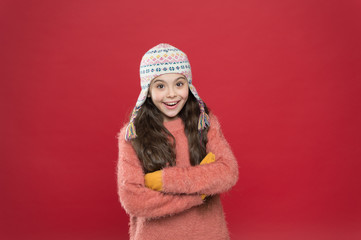 Frosty weather. Winter outfit. Cute model enjoy winter style. Small child long hair wear hat red background. Wintertime concept. Little kid wear knitted hat. Little girl winter fashion accessory