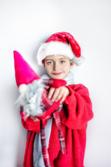 7 yaers old smiling smiling in santa hat, red pullover, gray scarf with dwurf in red hat on neutral background. Natural light. Space for text