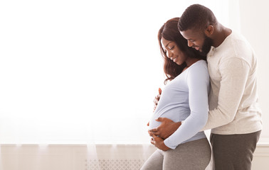 Pregnant woman and her husband embracing next to window