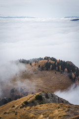 Dolomites, Italy - sunny day cloud inversion over hills with autumn colors on trees