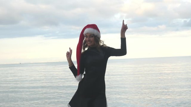 Funny woman in Santa hat funny dancing near the sea