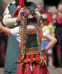 Little girl with long braids dances  in traditional costume from Krakow region, street folk events