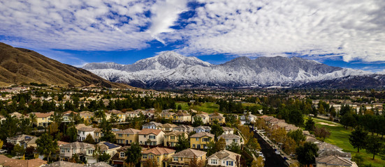 Aerial panorama of snow covered San Gorgonio and Little San Bernardino Mountains on a winter day above Yucaipa Valley with blue sky, white clouds, houses, hills