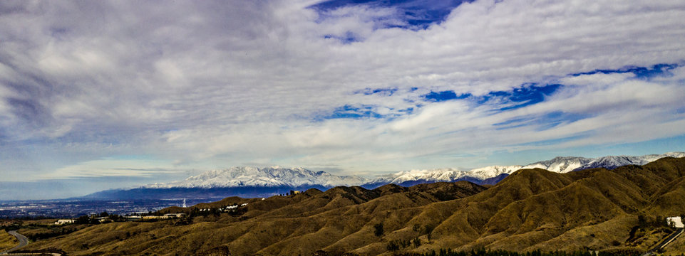 Panorama aerial view of the white snow covered San Gabriel and San Bernardino Mountains with Crafton Hills in the foreground with white clouds and blue sky