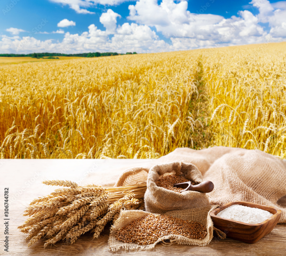 Sticker wheat ears, grains and flour on a wooden table on wheat field background