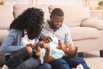 Loving afro parents tickling their little daughter, having fun at home