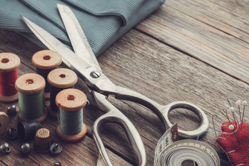 Retro sewing items: tailoring scissors, cutting knife, thimble, wooden thread spools, cushion for including pins, fabrics and sewing accessories. - obrazy, fototapety, plakaty