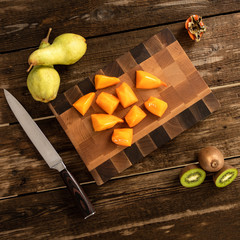 Obraz na płótnie Canvas Cut into pieces orange hurma using a knife on a wooden cutting board.