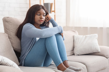 Lonely depressed african american woman sitting on couch at home