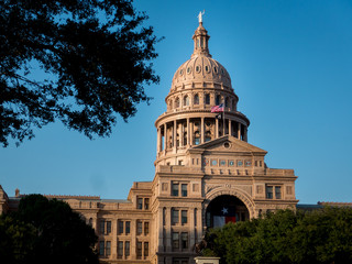 Texas capital in Austin with texas state flag, trees in foreground and clear blue sky