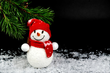 Snowman toy, Christmas balls, background with spruce branch, a group of elegant beautiful toys, on a black festive background with lights of lanterns and falling snow.