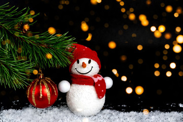 Snowman toy, Christmas balls, background with spruce branch, a group of elegant beautiful toys, on a black festive background with lights of lanterns and falling snow.