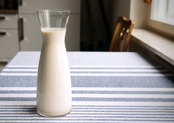 Fresh homemade oat milk in glass carafe standing on the kitchen table. Cozy atmosphere of interior, simply, plain healthy plant milk.Copy space.