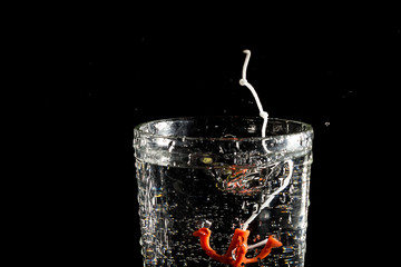 Red toy anchor on a white thread falling into a glass of water on a black background under studio lighting