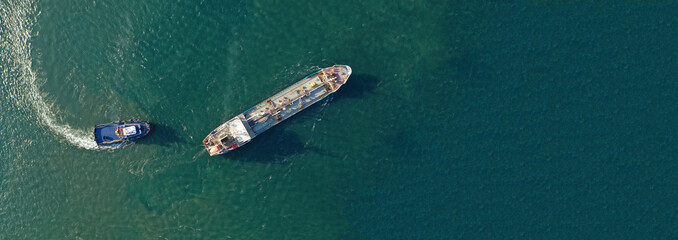 Aerial drone panorama photo of industrial fuel and gas tanker being towed by tugboat in bay and shipyard of Elefsina, Attica, Greece