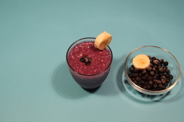 Blackberry and banana smoothie in glass with berries and fruit slices on blue background