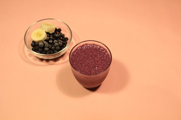 Blackberry and banana smoothie in glass, bowl with berries and fruit slices on pink background