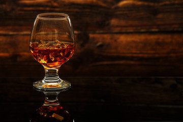 Whiskey with ice or brandy in a glass on a glass reflective surface. Whiskey with ice in a glass. Whiskey or brandy. Selective focus.