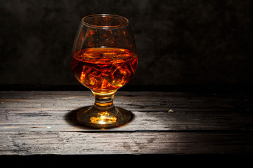 Whiskey with ice or brandy in a glass and a square carafe on an old wooden background. Whiskey with...