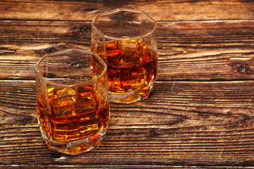 Whiskey with ice or brandy in a glass and a square carafe on an old wooden background. Whiskey with ice in a glass. Whiskey or cognac. Selective focus.