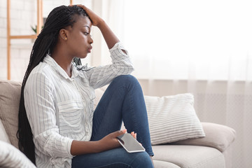 Upset Afro Girl Sitting On Couch With Cellphone, Thinking About Something - Powered by Adobe