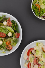 white deep plates with fresh salad ingredients mixed with sauce placed on an gray background. A place for a menu, banner or advertisement