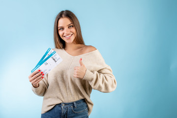 woman with boarding pass plane tickets showing thumbs up and smiling isolated over blue