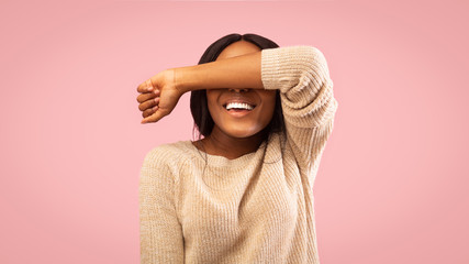 Smiling girl covering eyes with hand standing, pink background, panorama