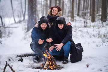 Happy friends warming next to a bonfire in the cold snowy forest