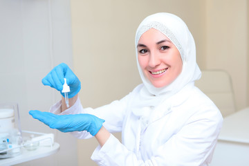 Beautician Muslim woman holding a dropper with a cosmetic composition. Portrait in national dress. Tolerance at work. Copy space.