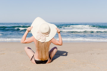 Fototapeta na wymiar Young woman sitting on a sea beach with hat. Summer vacation