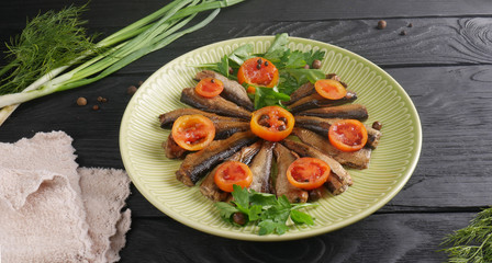 Sprats with chopped tomatoes, parsley and other green vegetables in a plate on a black wooden table
