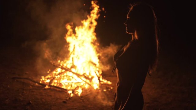 Silhouette of mystic woman in black background of fire fly flame, spark, of contour outline. Adult sexy of young girl witchcraft ceremony ritual dance in underclothes. Outdoor slow motion. Caucasian.