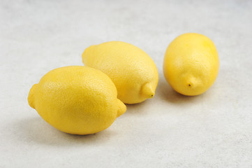 three whole yellow lemons on a gray surface