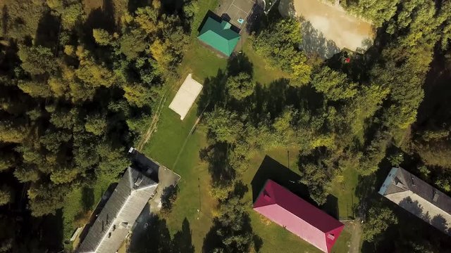 Aerial forest view at summer time in modern contryside area with beautiful houses, green trees and the river. Stock footage. Top view of buildings roofs, wooden pier and calm river.