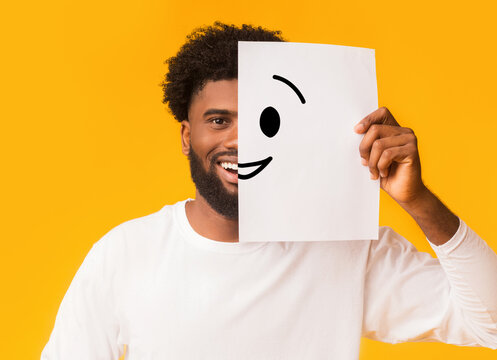 Black cheerful man covering half face with smiley picture