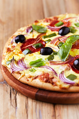 Pizza with salami, red onion, black olives and fresh basil. Rustic wooden background. 