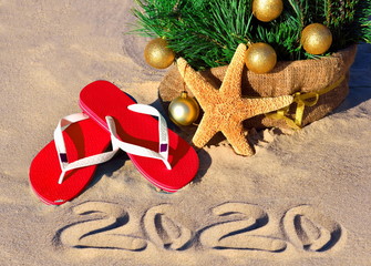 New Year 2020 on the beach. Christmas tree with christmas balls, slippers and starfish on the sand on beach