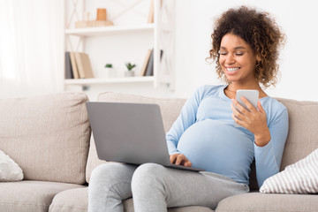 Happy expectant woman using technology devices at home