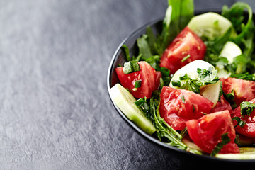 Salad with Tomatoes, Cucumber and Rocket on stone Background. Healthy Snack Idea. Close up. Copy space.
