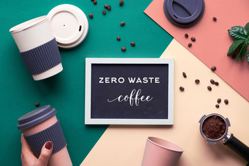 Zero waste coffee concept. Eco friendly reusable coffee cups in hands, geometric top view on split paper, creative background in green, beige and yellow with chalk text on black board.