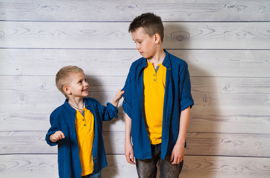 Two boys in casual clothes in white wooden background looking at each other. Two brothers posing. Elder and younger brothers. Happy childhood concept. Friendship.