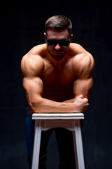 Fototapeta na wymiar Shirtless handsome male with a perfect muscular body posing while leaning on a chair in the studio.