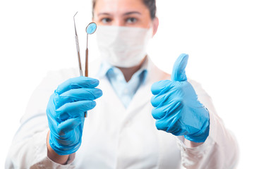 Oral dental hygiene. Female dentist doctor showing thumbs up and holding dentist mirror with explorer probe instrument in hands with blue rubber gloves