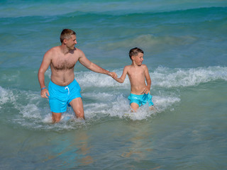 European man is happy to spend his summer holidays with his son. They are swimming in the ocean and enjoying pastime.